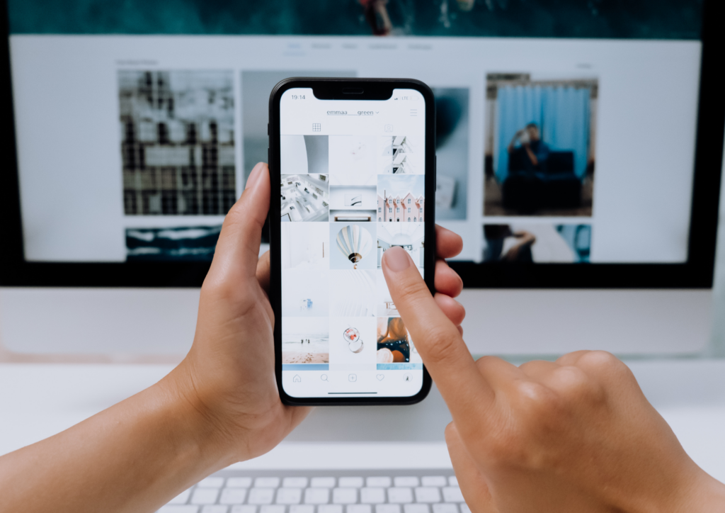 iemand die voor een computer zit en op zijn smartphone op Instagram aan het scrollen is.
