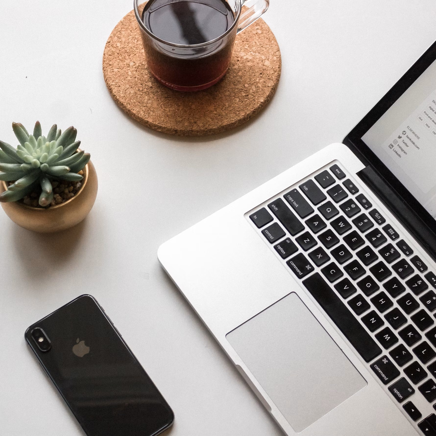 Een computer met een smartphone die op een tafel liggen, samen met en kop koffie en een plant